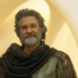 Kurt Russell med grått hår och skägg, klädd i en mörk sjal och rustning. En ikonisk skådespelare som syns i många filmer med Kurt Russell.