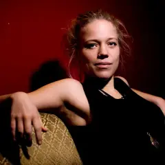 Olivia Bergdahl sitter avslappnat i en soffa, med en mörk bakgrund och en blick som fångar.