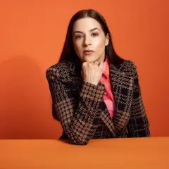 Nina de Geer sitter med hakan i handen, klädd i en rutig kavaj och en rosa skjorta.