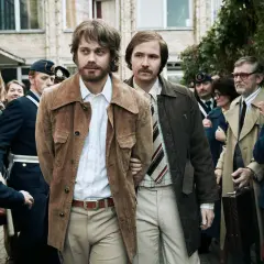 Två män förs till av poliser. En av dem, med bärnstensfärgad jacka, är Clark Olofsson i den hyllade clark olofsson serie.