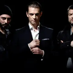 Tre män i mörka kläder poserar för snabba cash serie. En i kostym, en i jacka och en med mössa.