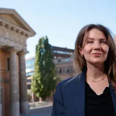 Cecilia Khavar ler mot kameran framför en klassisk byggnad med pelare.