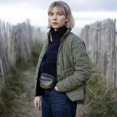 Karen Pirie står vid en vindpinad strand, klädd i en grön jacka och jeans. Hon bär en midjeväska, redo för ett nytt fall.