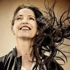 Kristina Sandberg ler mot himlen, håret fladdrar i vinden. En bild som fångar livets glädje, kanske en hyllning till Kristina Sandbergs familj.