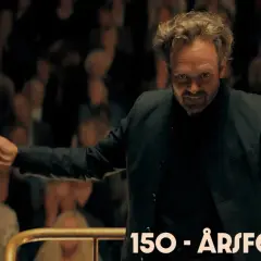 Dirigenten leder orkestern med passion, som om han vore med i rollistan i Hugo Cabret. Publiken ser på.