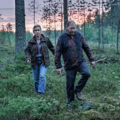 Två personer går genom en skog i skymningen. Det är en scen från Vargasommar del 2.