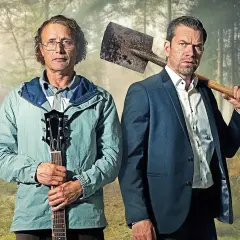 Två män i skogen, en med gitarr, en med spade. En scen från en mads mikkelsen serie.