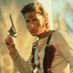 En ung man med smuts i ansiktet och blodfläckar på skjortan håller en revolver. Han är en del av rollistan i Young Guns.