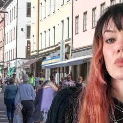 En kvinna med rosa hår poserar framför en livlig svensk stadsgata. Kanske är hon på väg att ta "little jinder expressen" till nästa äventyr.