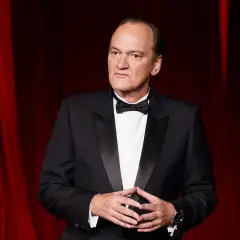 Quentin Tarantino, ikonen bakom ikoniska tarantino filmer, i en elegant smoking framför en röd ridå.