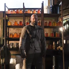 Jason Statham som rollistan i The Beekeeper, omgiven av burkar med honung och jordbruksutrustning.