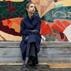 Alexandra Andersson sitter på en träbänk framför en färgglad mosaikvägg.