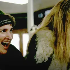 En glad kvinna med grön mössa och en annan kvinna med blont hår som äter ett körsbär. Scen från "Girl, Interrupted" (Stulna år).