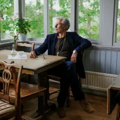 Carl-Johan Vallgren, med sin fru vid sin sida, sitter vid ett bord med utsikt över en grönskande trädgård.