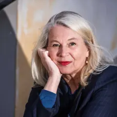 Helena von Zweigbergk, med sin partner vid sin sida, ler mot kameran. Hennes blonda hår ramar in ett ansikte med röda läppar och en pärlörhänge.