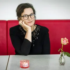 Agnes Lidbeck med familj, en kvinna med glasögon och en blomma på bordet, sitter vid ett rött bås.