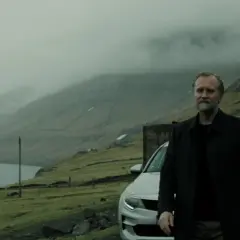 En man med grått skägg står vid en bil i ett dimmigt, bergigt landskap. Han ser ut att vara en del av rollistan i "Trom".