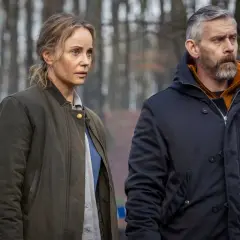 Två personer, en kvinna och en man, står i en skog. Bakom dem syns blåvit avspärrningsband. Kanske är det Sandor Berg som utreder ett brott.