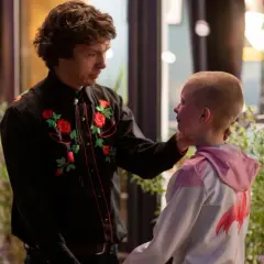 En man med blommig skjorta rör vid ett barns kind. En scen som kan ingå i svenska komedier.