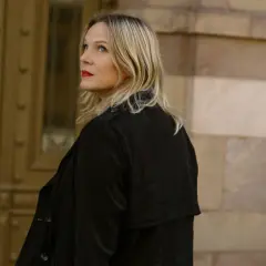 Jenny Aschenbrenner, med rött läppstift och blont hår, tittar uppåt mot en byggnad i sten.