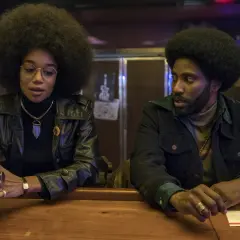 En kvinna med stor afro och en man med skägg sitter vid en bardisk. De är medlemmar i rollistan i Blackkklansman.