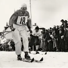 En skidåkare med nummer 18 tävlar i den vita sporten, publiken hejar.