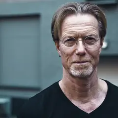 Porträtt av Emil Eiman Roslund med glasögon och skäggstubb, klädd i svart t-shirt.