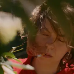 En ung kvinna med rufsigt hår, med slutna ögon och en cigarett i munnen, som en del av rollistan i Sameblod.