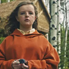 Charlie i orange hoodie, med en fågel i händerna, framför ett trädkoja i skogen. En scen från rollistan i Hereditary.