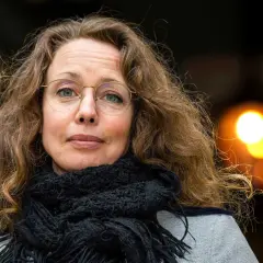 Sara Gordan dotter med sitt långa, lockiga hår och en svart halsduk. Hon bär glasögon och tittar rakt in i kameran.