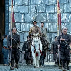 En ståtlig shogun på vit häst, omgiven av sina samurajer, anländer till en befästning. Scen från shogun serie.