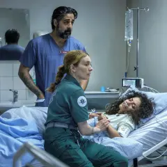 Två vårdare övervakar en patient i en sjukhussäng. En av dem håller patientens hand. Scen från en vaka serie.