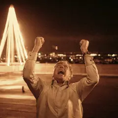 Man jublar med knutna nävar mot en upplyst julgran och stad i bakgrunden. Känslan av riket exodus infinner sig.