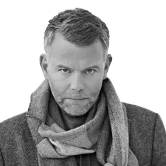 Jan Arnald, med gråmelerat hår och skägg, bär en tweedkavaj och halsduk. Kanske en scen från filmer med Jan Arnald.