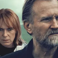 Två ansikten, en kvinna med rött hår och en man med grått skägg, tittar ut över ett dimmigt landskap. En scen från en spännande trom serie.