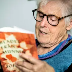 Äldre kvinna med glasögon läser en bok med titeln "Blad från munnen" av Elsie Johansson Thore.