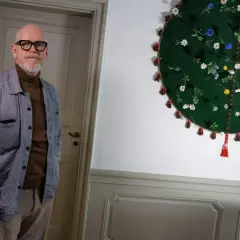 Jonas Axelsson, en man med glasögon och skägg, står bredvid ett runt, grönt konstverk med blommor och tofsar.