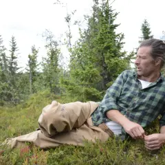 Frida Torgeby vilar i skogen, omgiven av blåbärsris och granar.