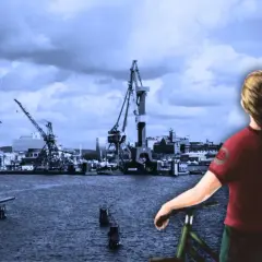 Karin Hallberg står vid en cykel och blickar ut över en hamn med kranar och byggnader.