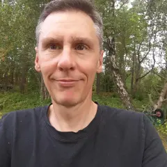 Johan Nilsson ler mot kameran i en skogsmiljö med träd och buskar.