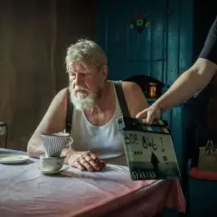 Rolf Lassgård sitter vid ett bord med en kaffebryggare. En person håller upp en filmklappa för en ny serie med Rolf Lassgård.