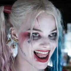 Margot Robbie som Harley Quinn, med sitt karaktäristiska smink och frisyr, ler galet.
