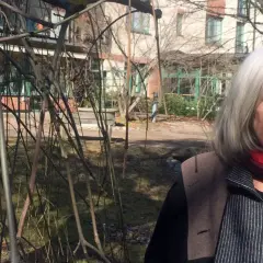 Agneta Pleijel ung, med grått hår och röd halsduk, ler mot kameran i en trädgård.