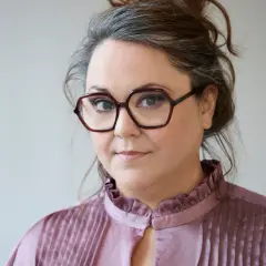 Malin Haawind med glasögon och en rynkad krage på en ljus bakgrund.