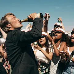 Mads Mikkelsen dricker ur en champagneflaska, omgiven av glada studenter med studentmössor. En runda till recension av firandet.