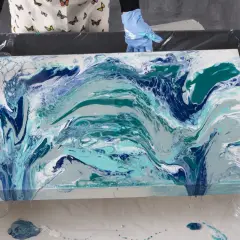 En person med blå handskar skapar en virvlande resin art-målning i blå och turkosa nyanser.