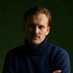Pascal Engman, med mustasch och mörk polotröja, poserar framför en mörkgrön bakgrund.