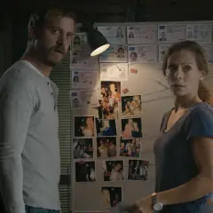 Två utredare, en man och en kvinna, tittar på en vägg med foton och ID-kort. Kanske en ledtråd i fallet med nya Maria Wern.