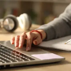 Personens händer arbetar vid ett skrivbord, en på en laptop, den andra skriver i en anteckningsbok. Perfekt för en skrivarkurs helg.