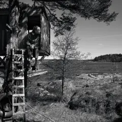 Man i trädkoja vid havet, som hämtad ur en berättelse av John Ajvide Lindqvist. Barnens lekplats blir en plats för eftertanke.